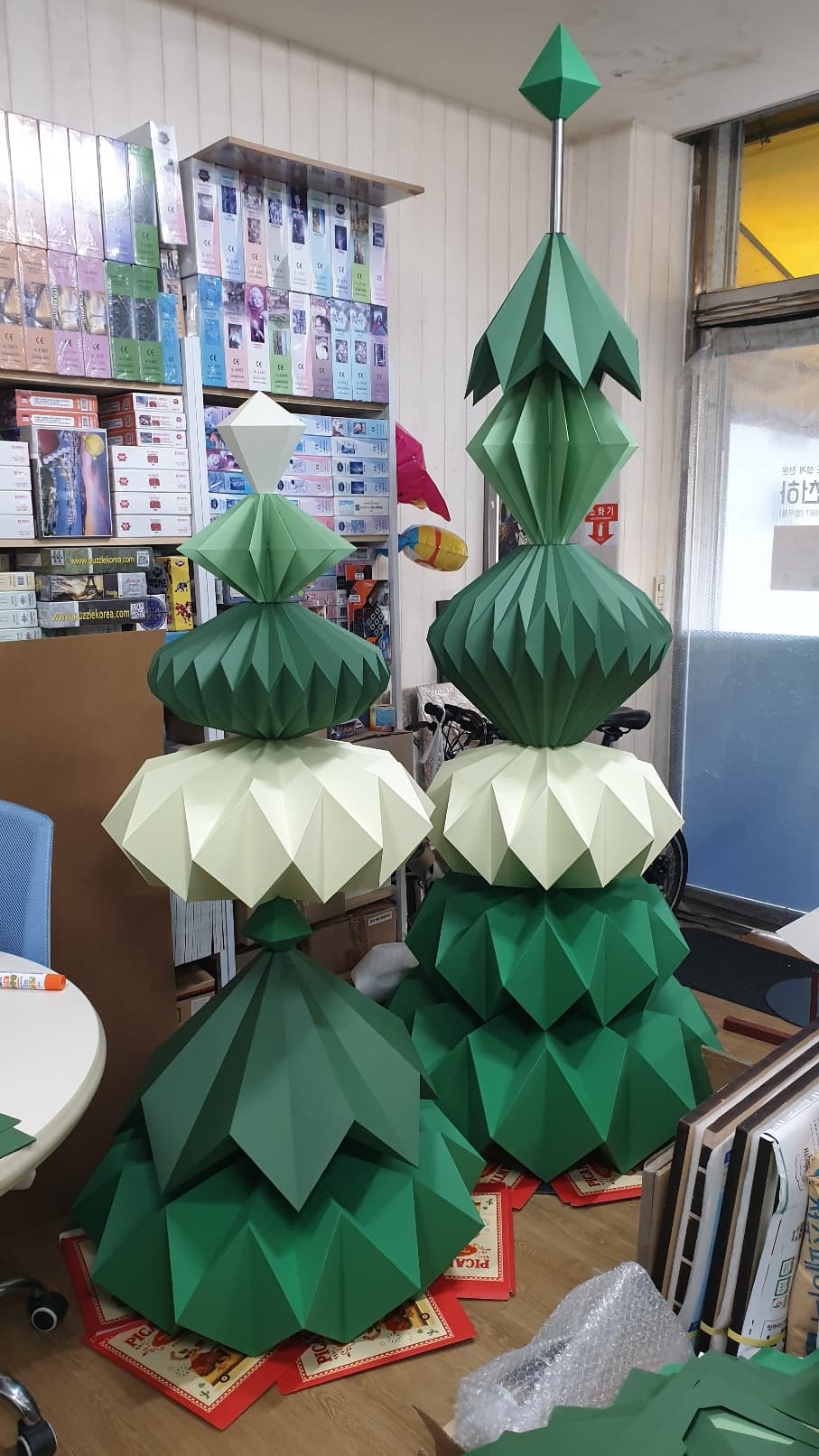 작업실 바닥에 세워 둔 사람 키를 넘는 초록 페이퍼 오브제 두 기둥, 다이아몬드형과 등불형 유닛이 번갈아 쌓였다