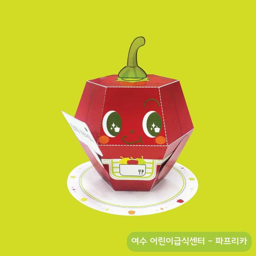 연두색 배경의 종이 접시 위에 놓인 빨간 파프리카 액션 페이퍼토이, 초록 꼭지와 반짝이는 큰 눈에 주황 볼터치가 귀엽다