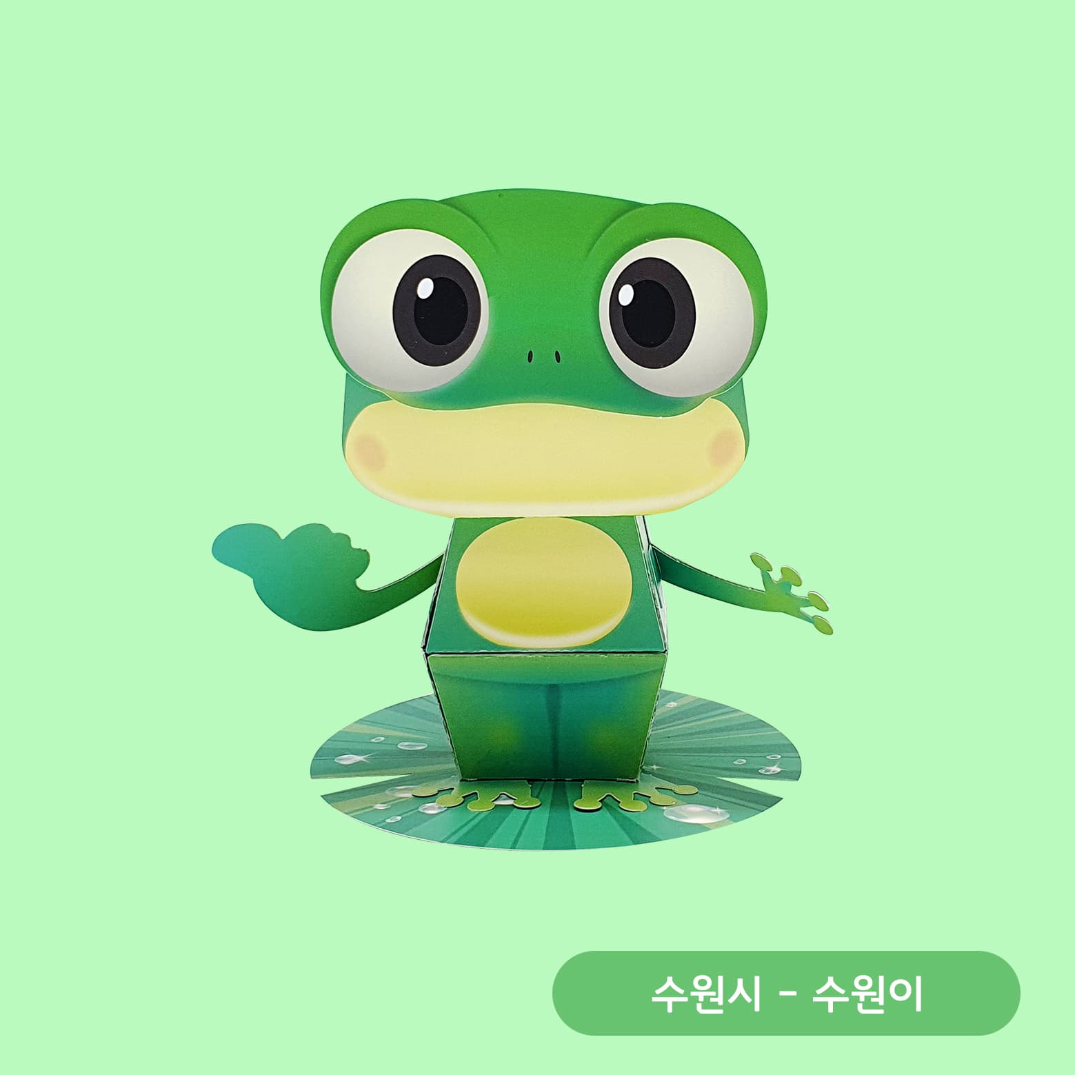 커다란 눈망울의 초록 청개구리 수원이가 한 손을 들어 인사하며 물방울 그려진 연잎 받침 위에 선 페이퍼토이