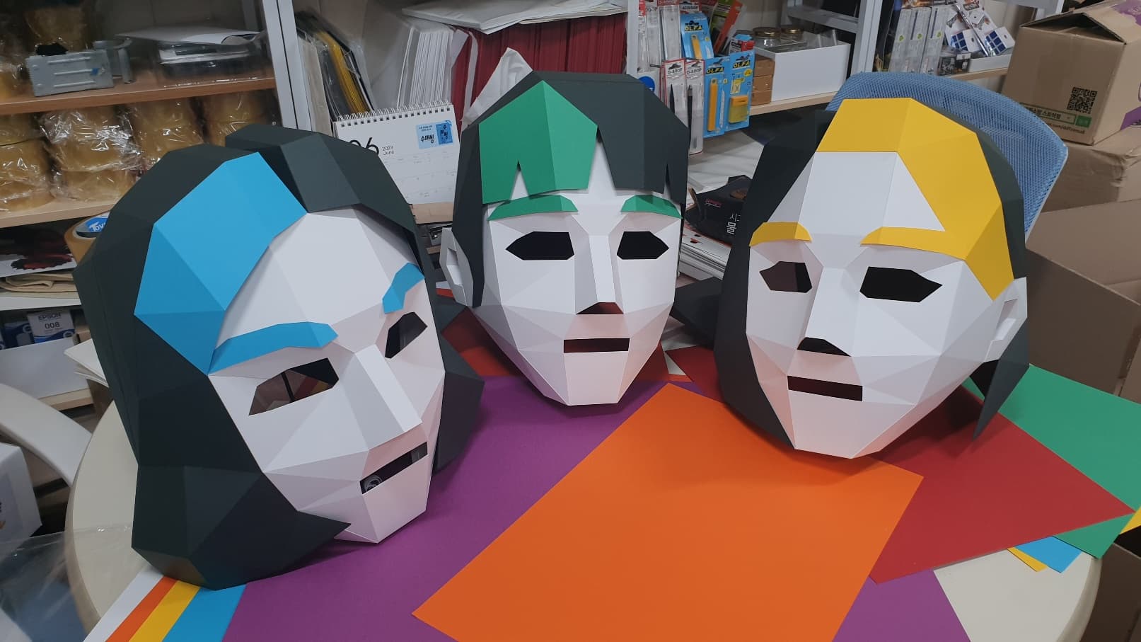 하늘색·초록·노랑 앞머리를 하나씩 다르게 입힌 페이퍼 마스크 세 개가 색종이 위에 나란히 놓여 서로 구분된다