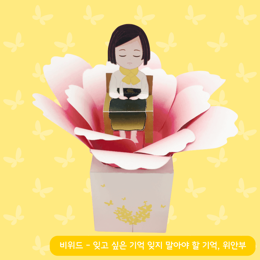 나비 무늬 노란 배경 앞 정면에서 본 소녀상 페이퍼토이, 분홍 꽃잎 가운데 고개 숙인 소녀와 금빛 나비 무늬 상자