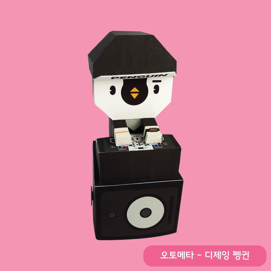 PENGUIN 글자가 박힌 검은 모자를 쓴 펭귄이 믹서 위에 두 손을 올리고, 아래에는 커다란 우퍼 스피커 박스가 놓인 오토마타 페이퍼토이