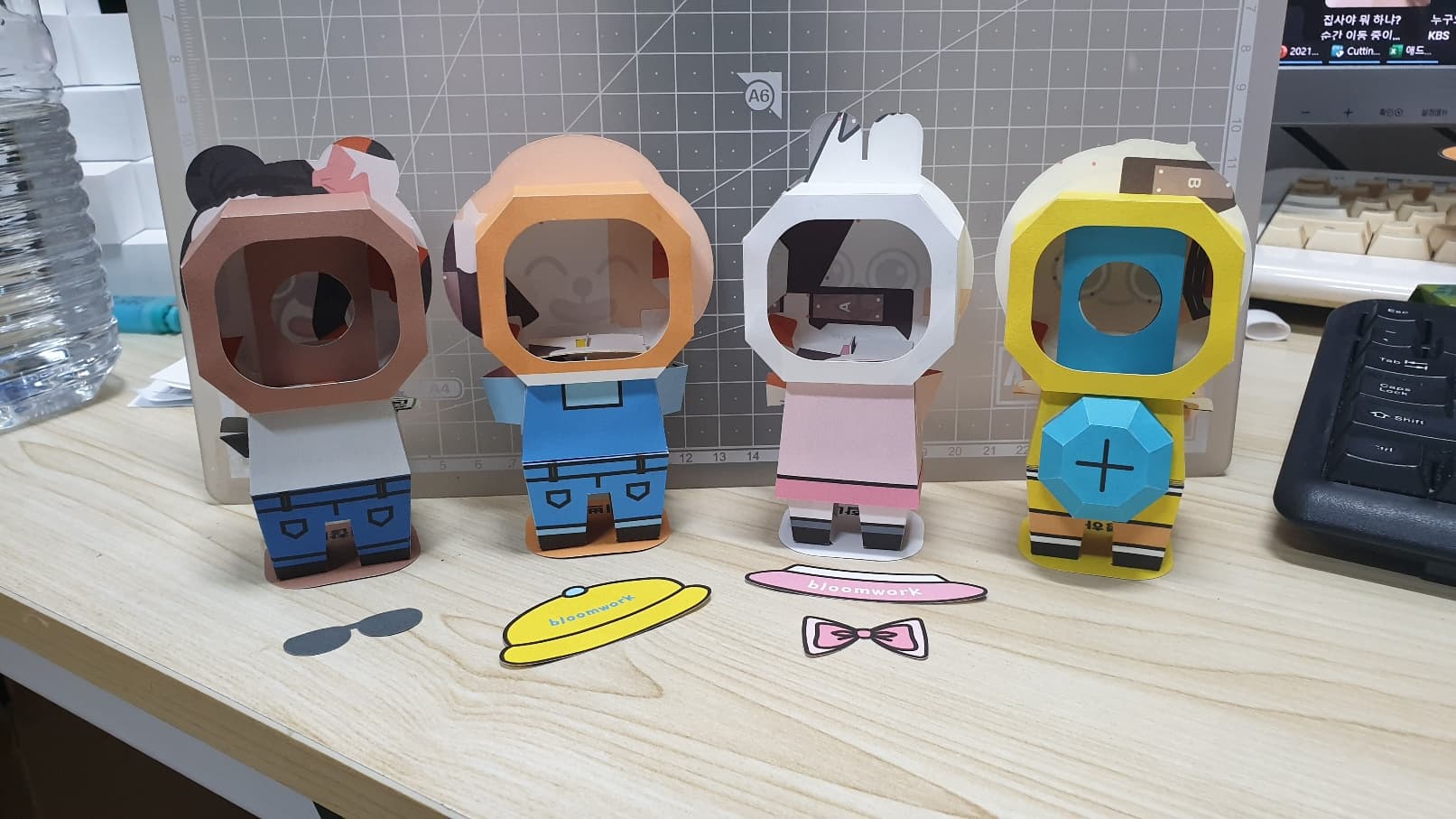 머리 뒷면에 손가락을 넣는 큰 구멍이 뚫린 네 캐릭터의 뒤쪽과 그 앞에 늘어놓인 노란 모자·분홍 리본 꾸미기 파츠