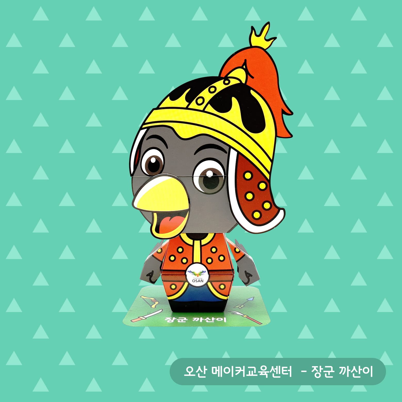 노란 투구에 붉은 깃털을 꽂고 주황 갑옷을 두른 장군 까산이가 삼각무늬 배경 앞 초록 받침대에 선 페이퍼토이