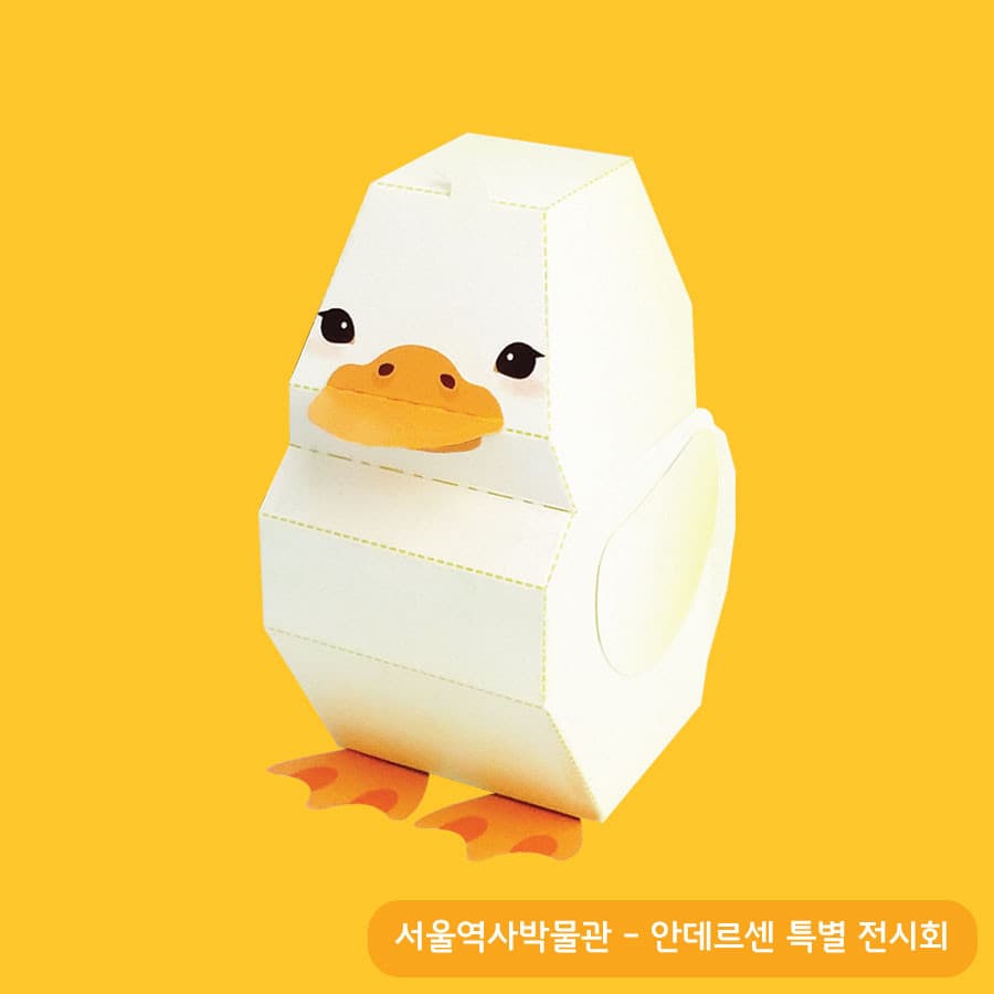 노란 배경 위에 흰 몸통과 주황 부리, 넓적한 물갈퀴가 도드라지는 오리 페이퍼토이, 접는 선이 점선으로 남아 있는 종이 질감